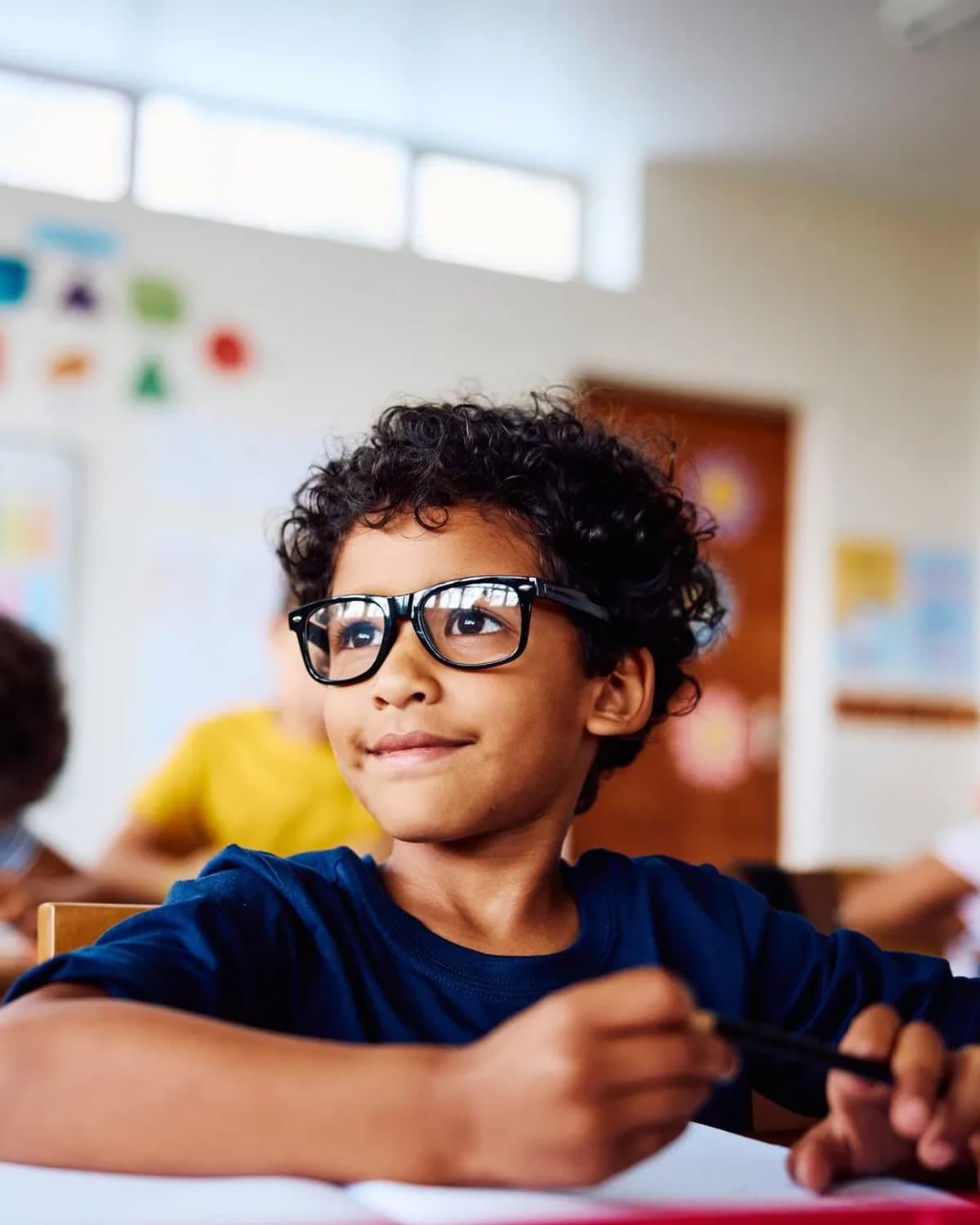 A primary school pupil at his desk, looking up towards the front of the classroom